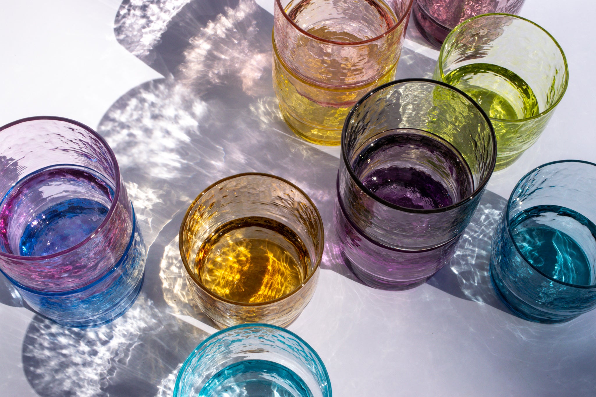 Colorful glass tumblers filled with different colored liquids on a reflective surface